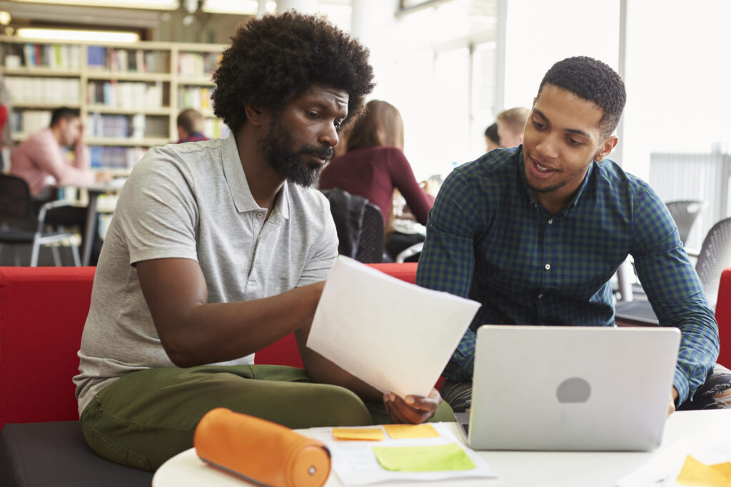 Male University Student Working In Library With Tutor