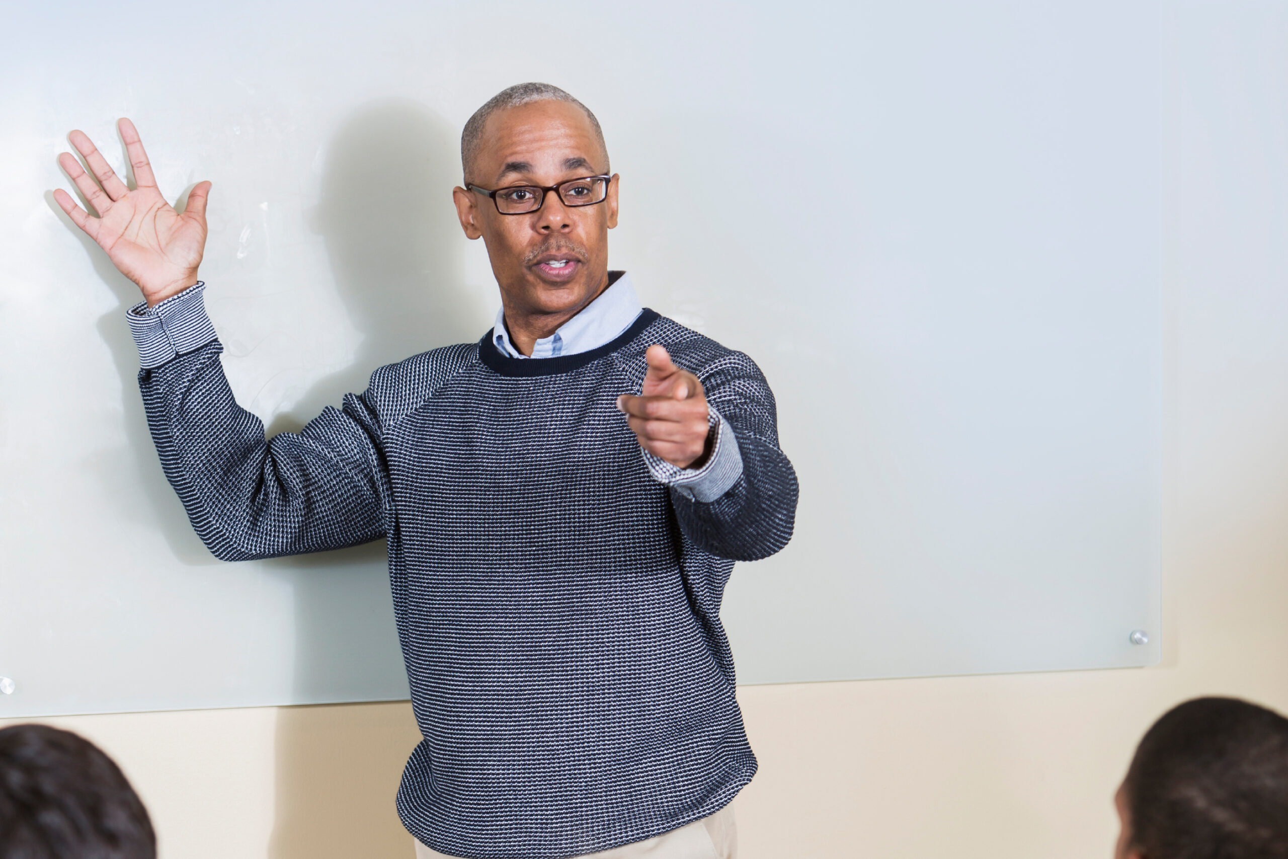 Mature African American man (50s) in front of class of high school or college students using digital tablets.